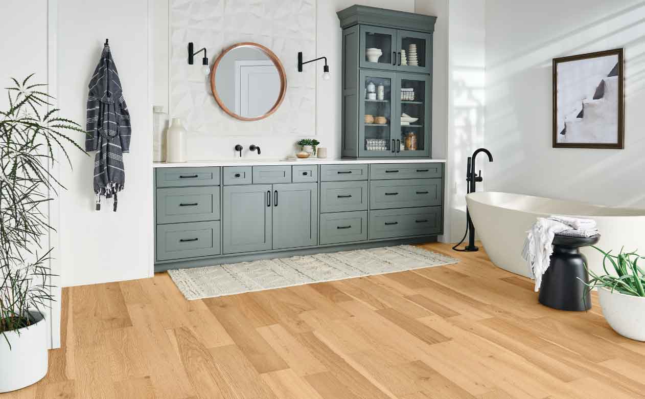 Light Hardwood Flooring in Bathroom, Grey Cabinets, mirror, bathtub, and rug